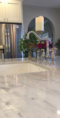 Marble kitchen island with sink, stainless fridge, and flowers beneath an arched mirror