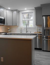 Modern kitchen with gray cabinets, stainless steel appliances, island, and window over the sink