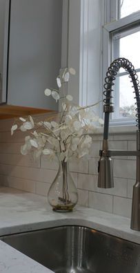 White flowers in a glass vase on a kitchen counter beside a sink and faucet by a window