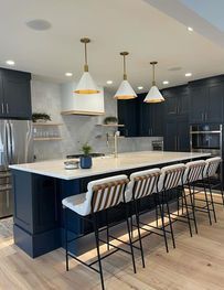 Modern kitchen with navy cabinets, white island, pendant lights, and striped bar stools.