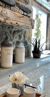 Cozy mantel with two white bottles, a potted plant, and decor beside a window and marble countertop