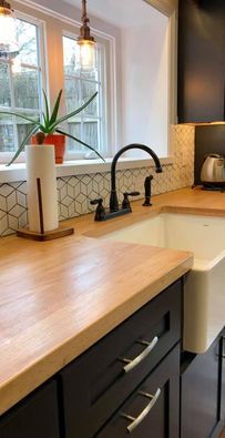 Modern kitchen sink and countertop with black faucet, white backsplash, and a potted plant by the window