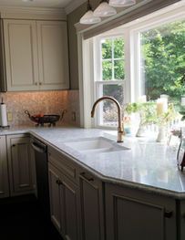 Bright kitchen with marble island, chrome faucet, cream cabinets, and a window overlooking greenery