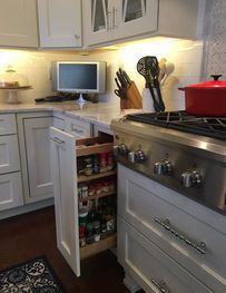 Kitchen with open lower cabinet revealing pantry shelves beside a stove with a red pot.