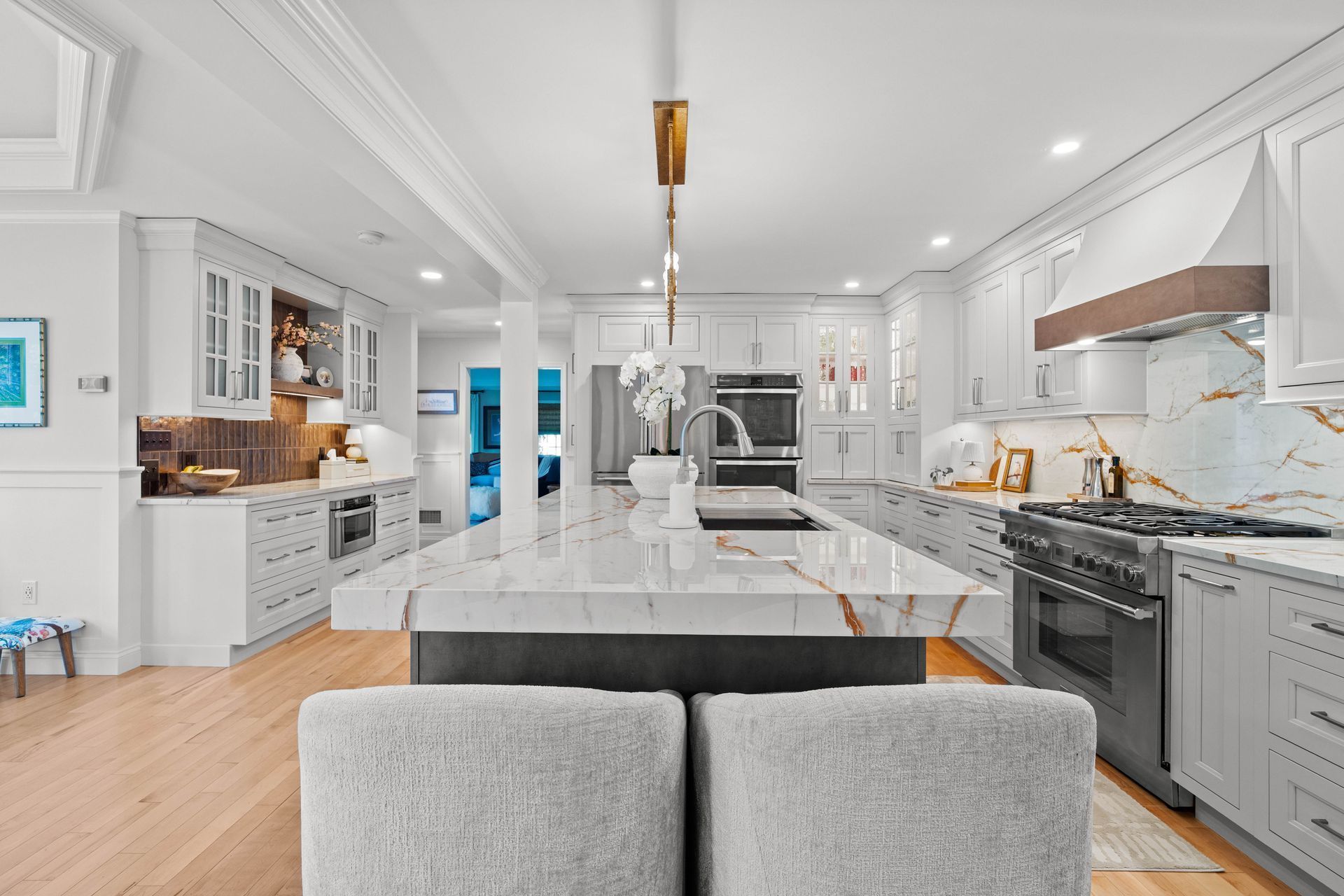 Bright modern kitchen with large marble island, white cabinets, and gray seating