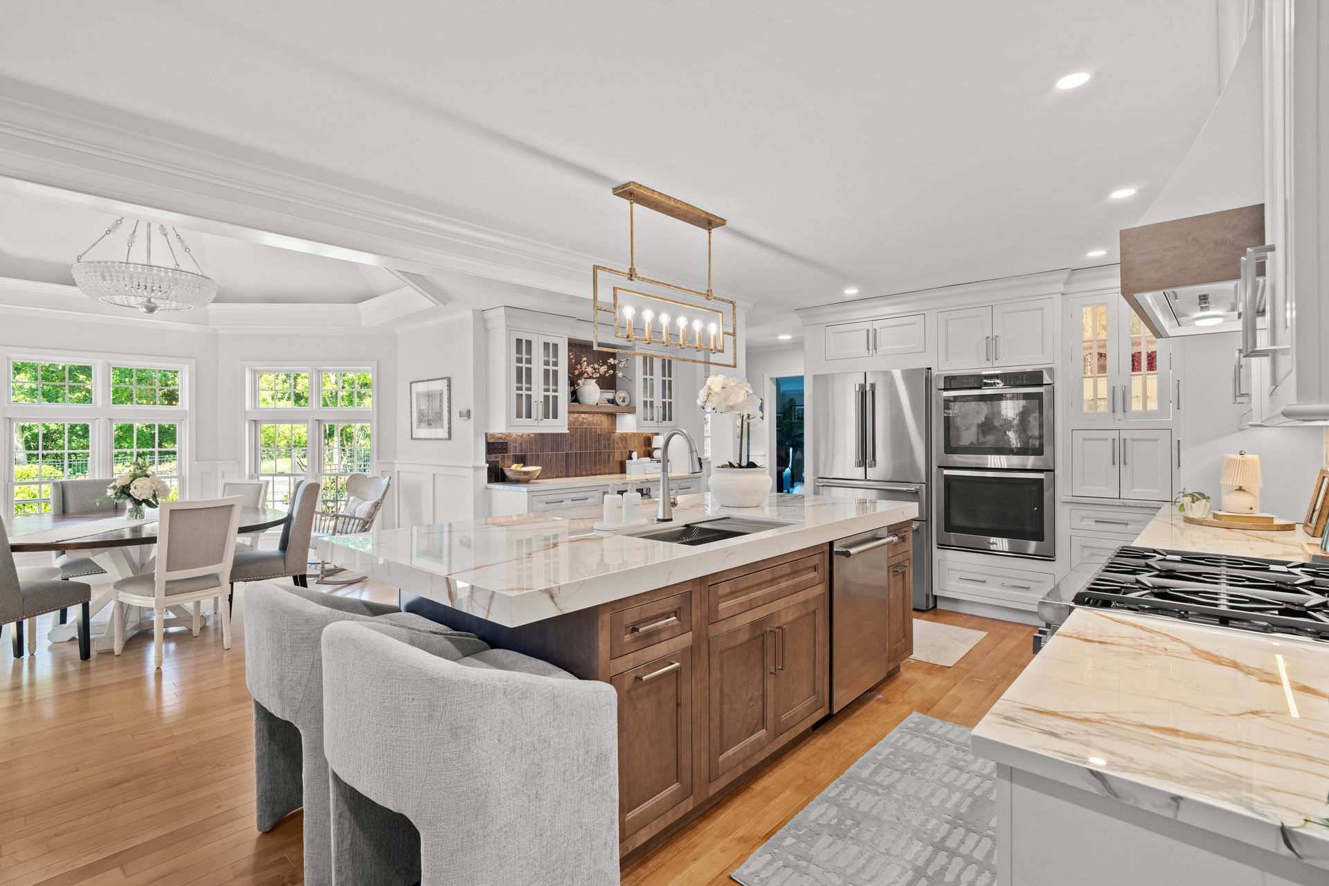 Bright modern kitchen with white cabinets, marble island, gray stools, and stainless steel appliances