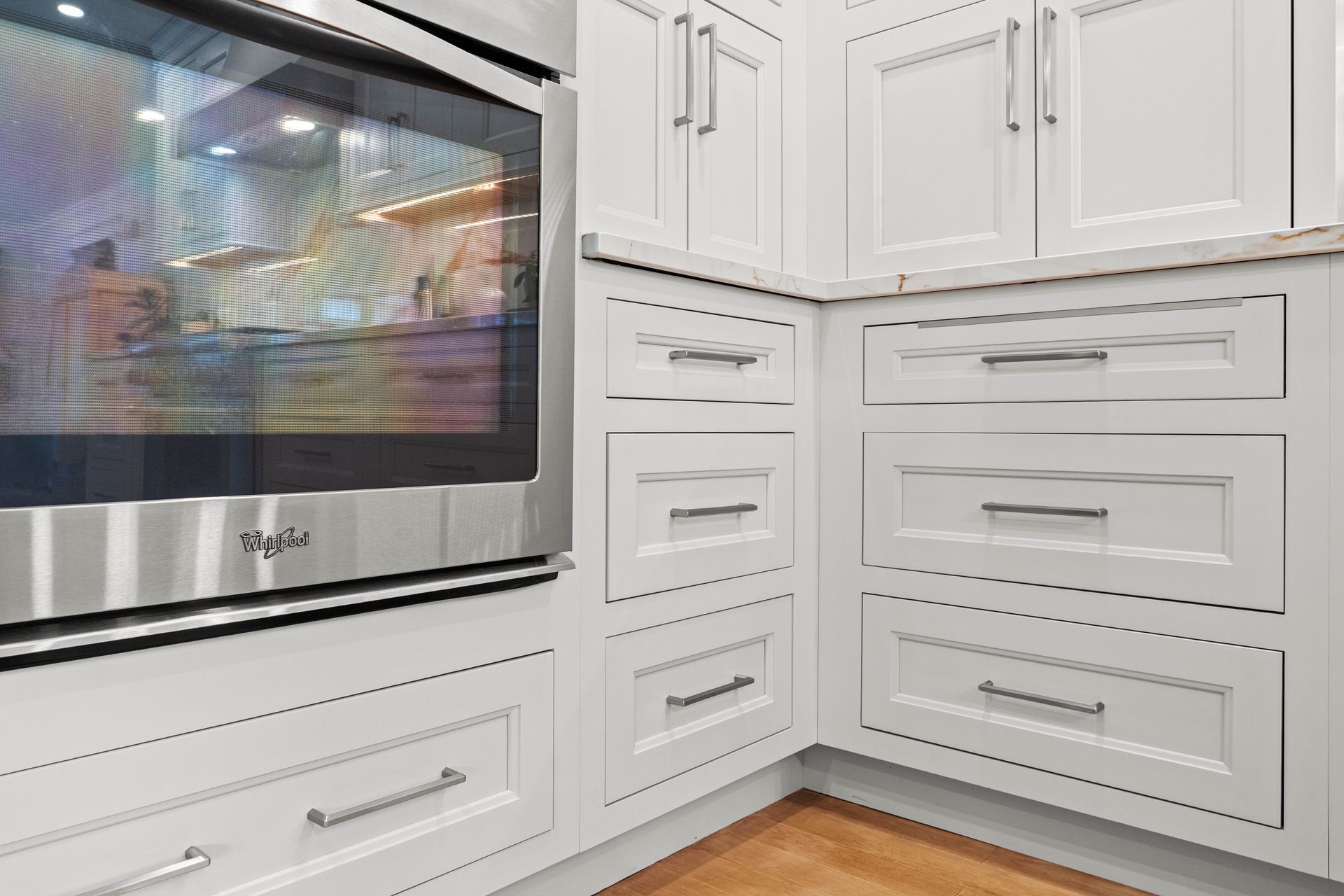 White kitchen cabinets beside a stainless steel oven and microwave, with wood flooring.