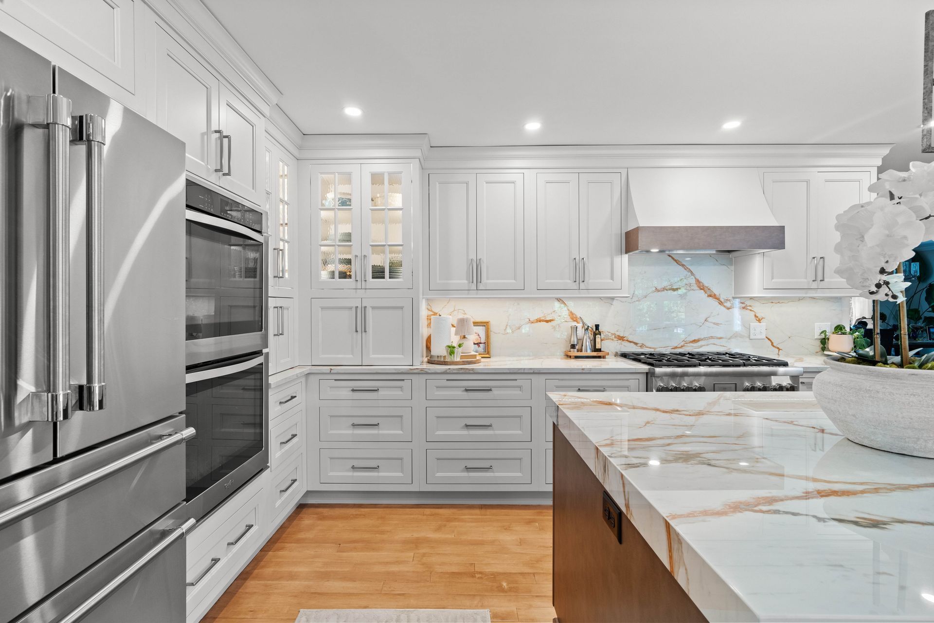 Modern white kitchen with stainless steel appliances, marble counters, and light wood floors
