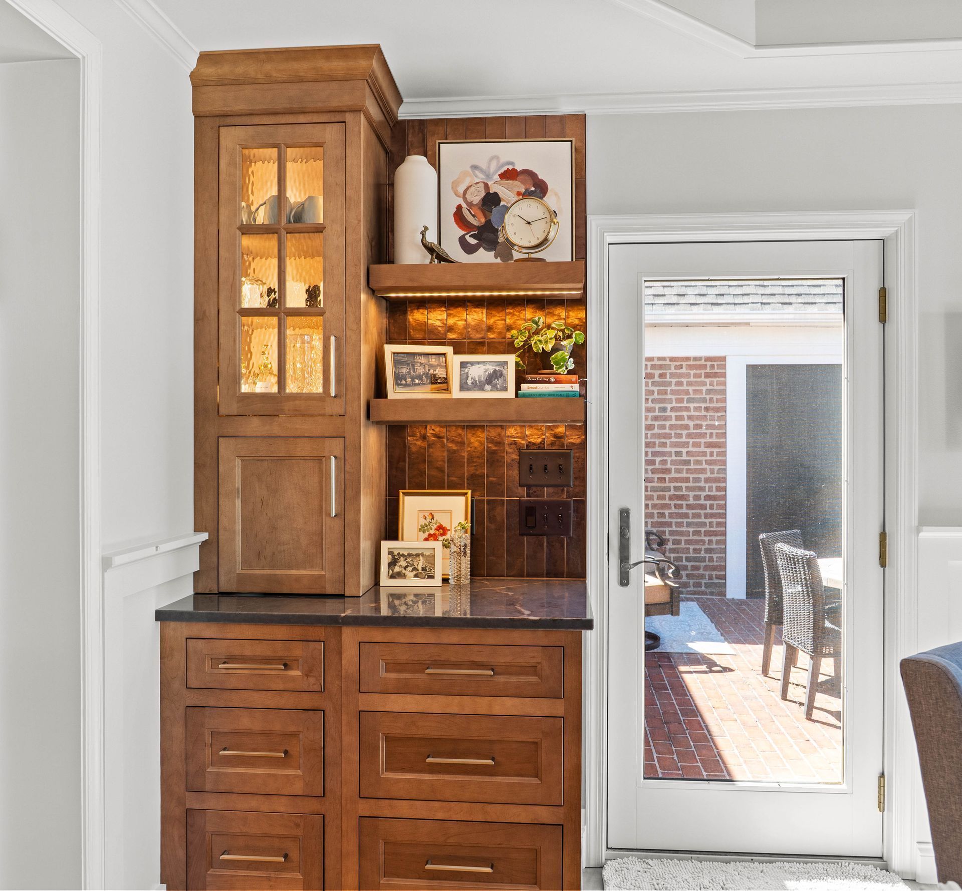 Wooden kitchen cabinet hutch beside a glass door, with shelves displaying decor and framed art.