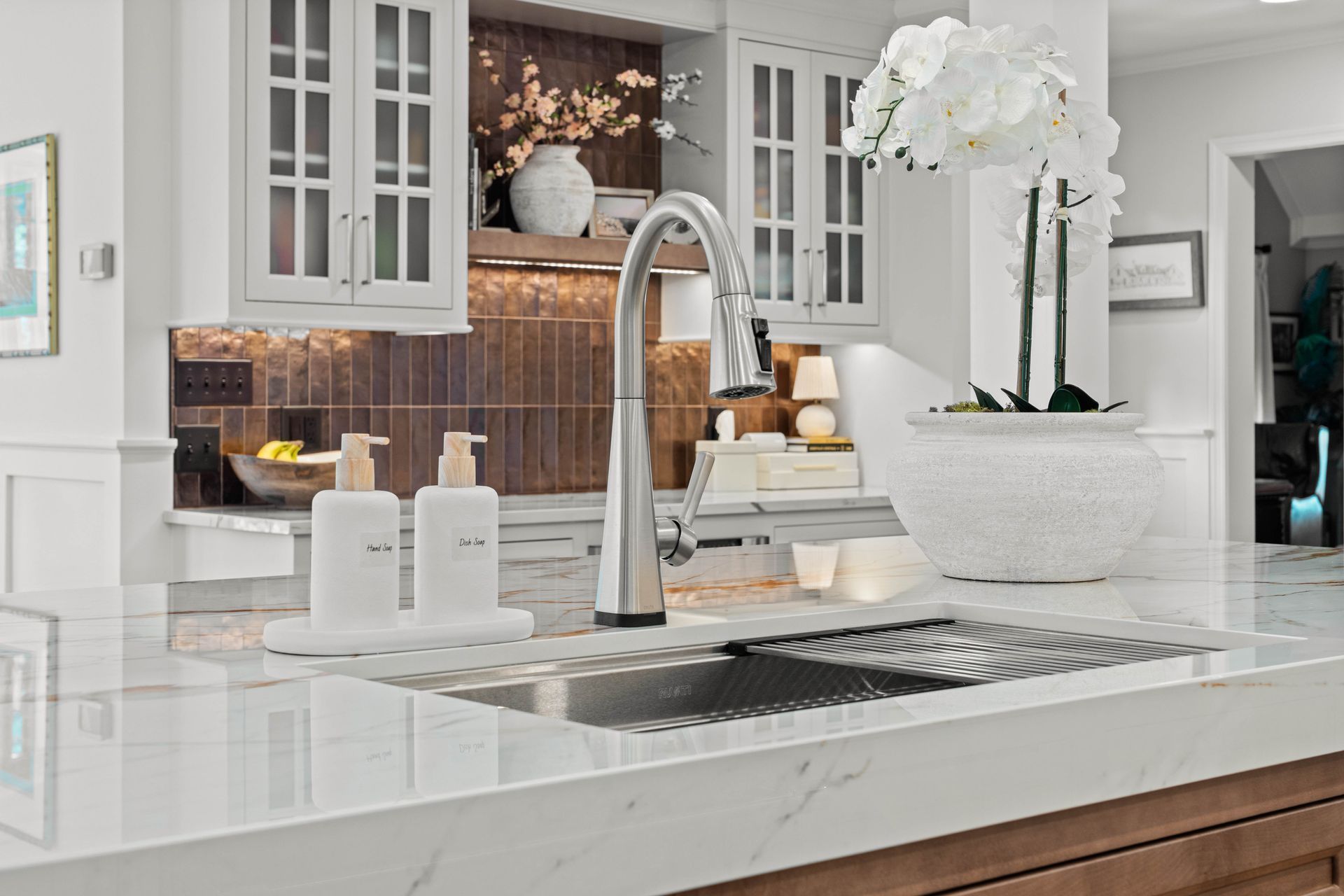Modern white kitchen with marble island, chrome faucet, sink, and white orchid centerpiece