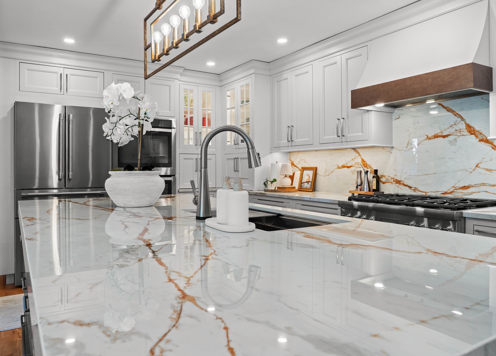 Bright white modern kitchen with marble island, gold veining, stainless fridge, and black range.
