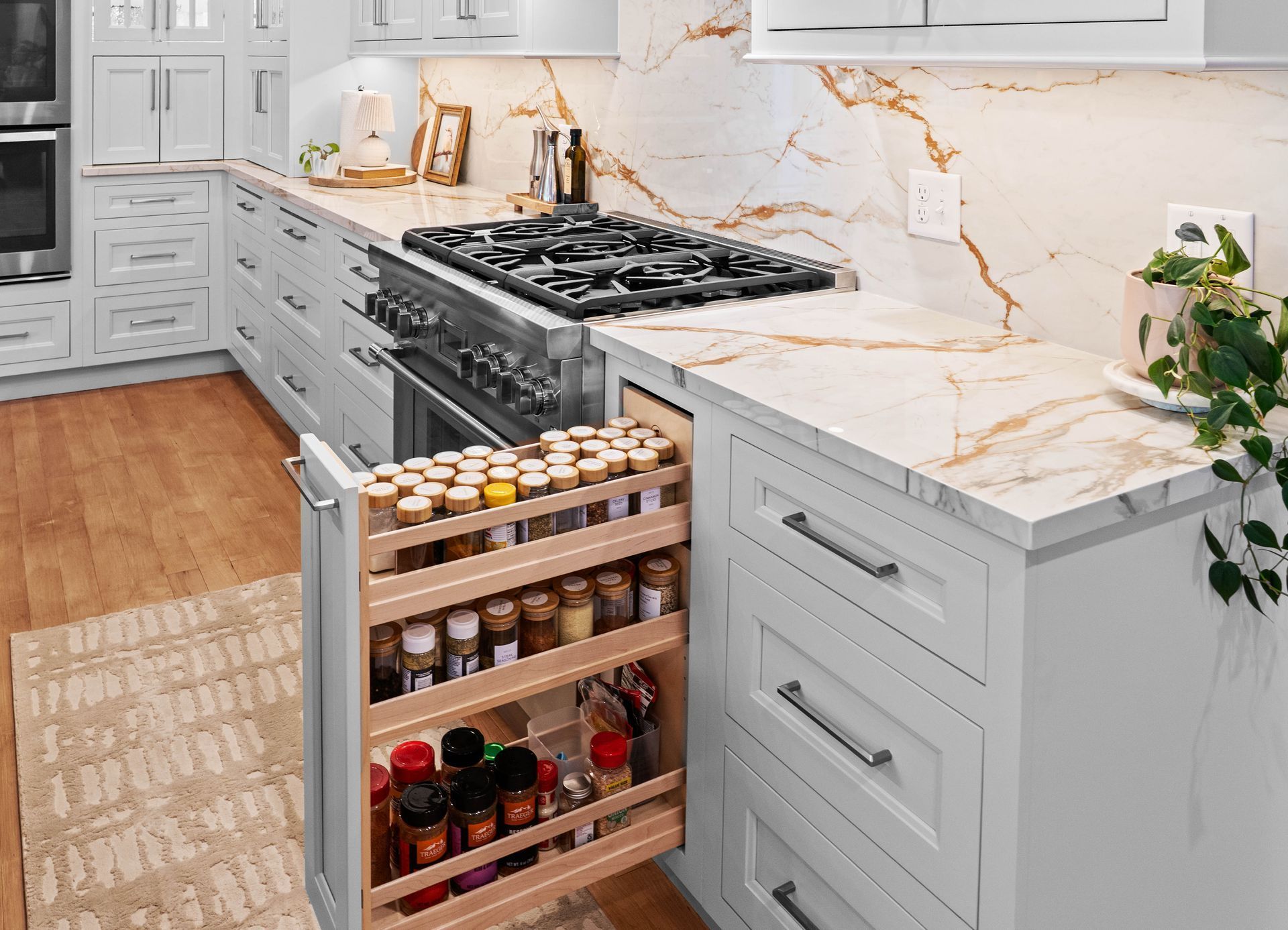 Modern white kitchen with marble island and pull-out spice rack beside a stainless stove.