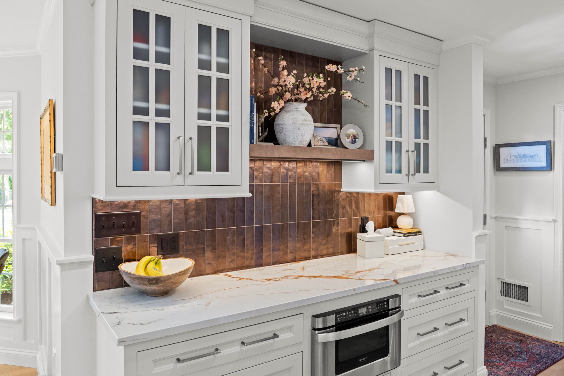 Bright kitchen with white cabinets, brown tile backsplash, and built-in oven under a countertop.