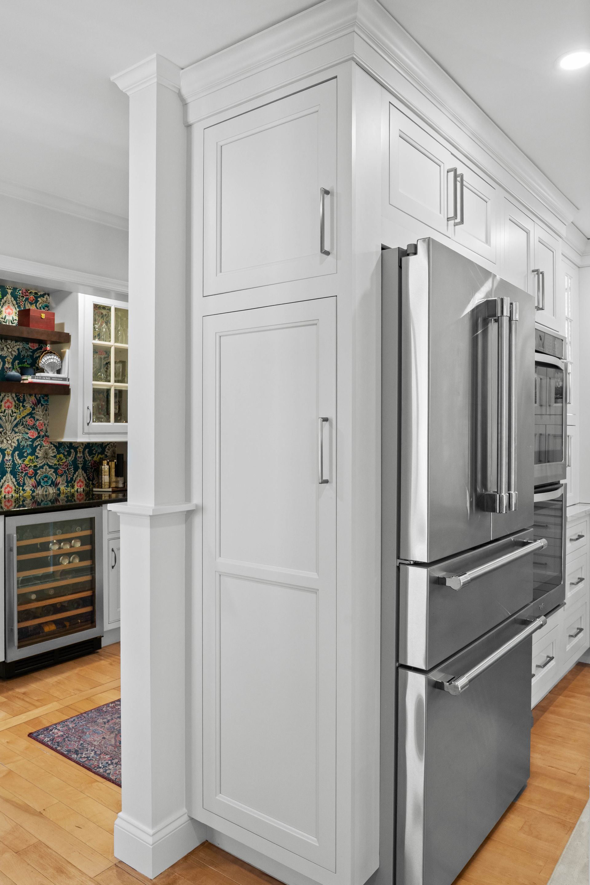 White kitchen pantry cabinets beside a stainless steel refrigerator in a bright modern home