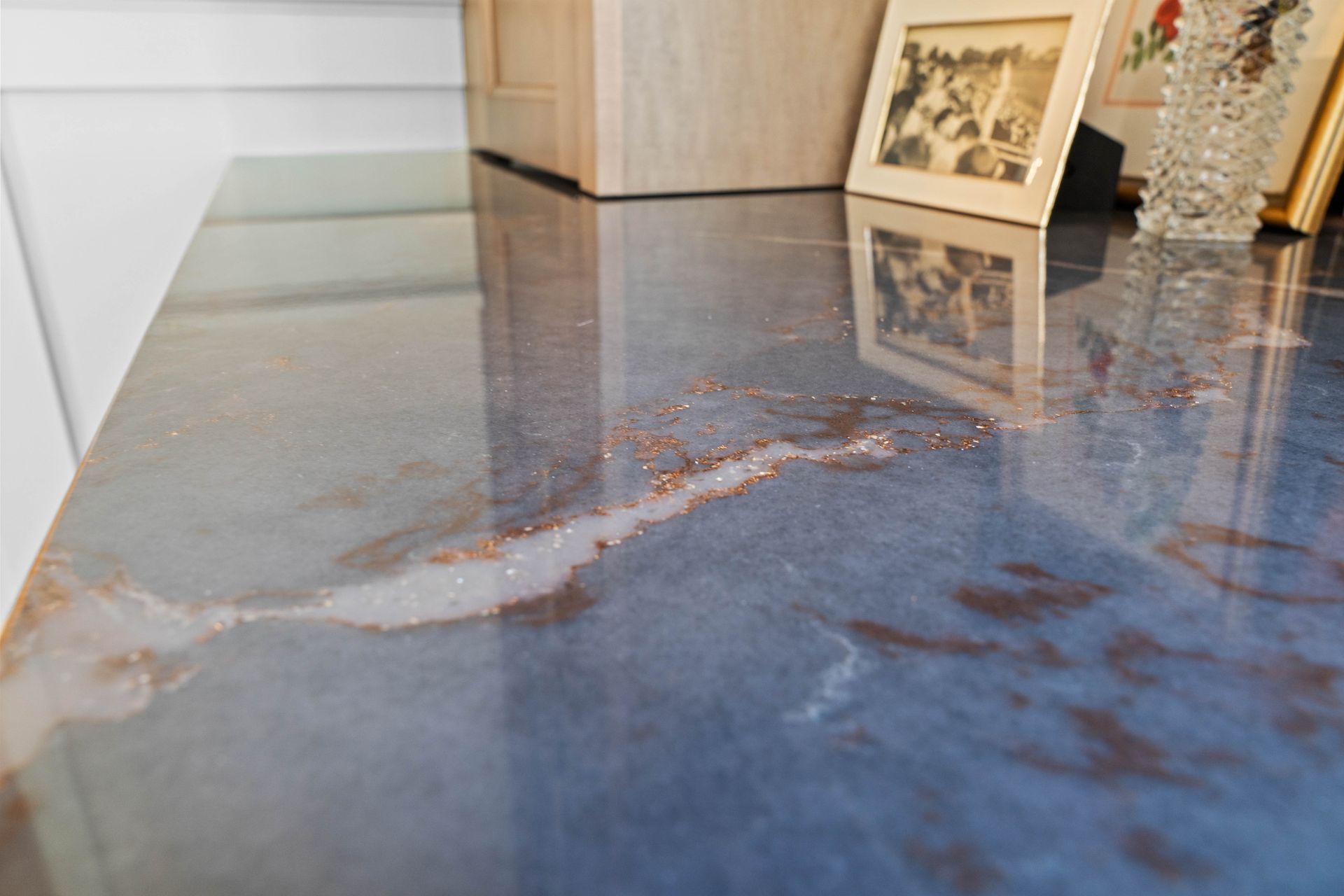Glossy blue epoxy floor with a resin river design, reflecting framed artwork in a modern interior