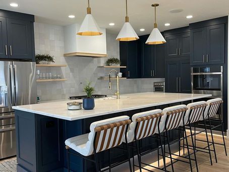 Modern kitchen with navy cabinets, white island, and four striped bar stools under pendant lights