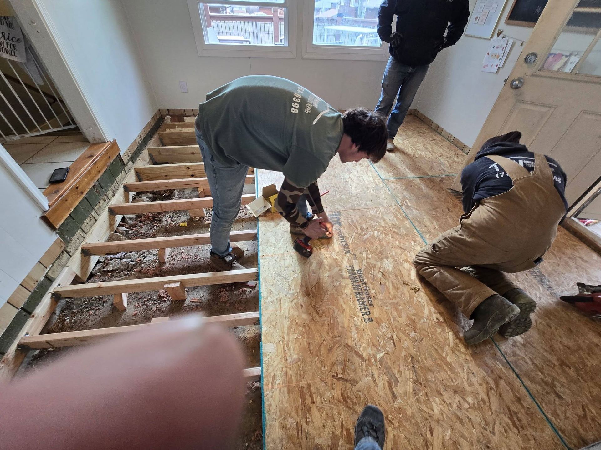 Men installing wood flooring in a room with a partially constructed staircase.