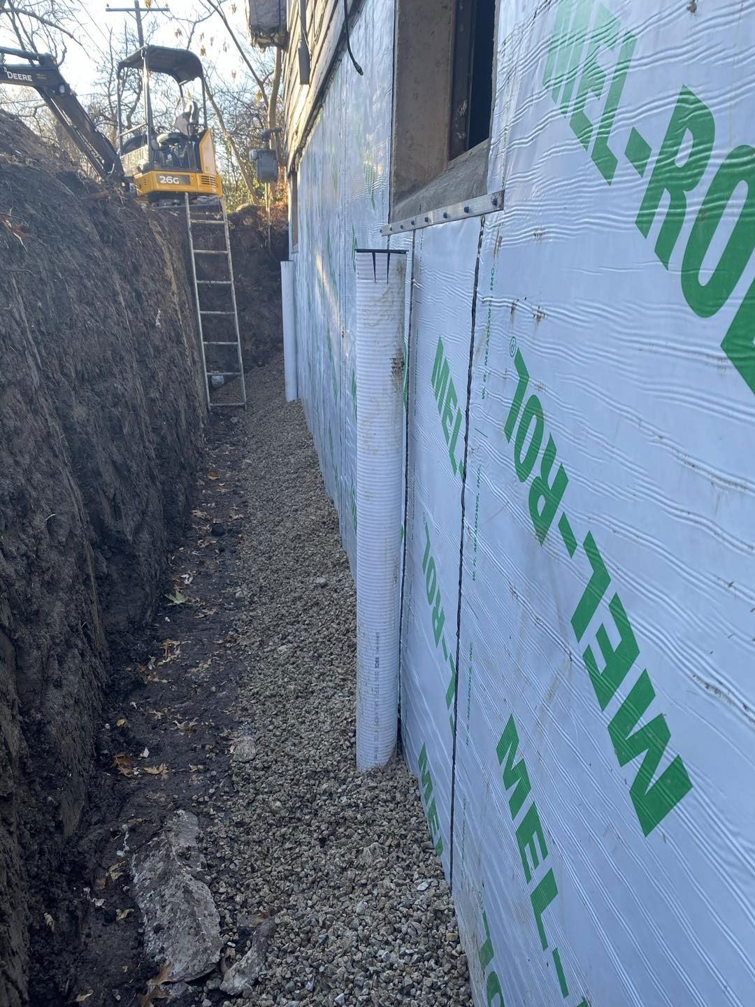 Foundation waterproofing in progress: a trench next to a house, with drain tile and waterproof membrane installed.