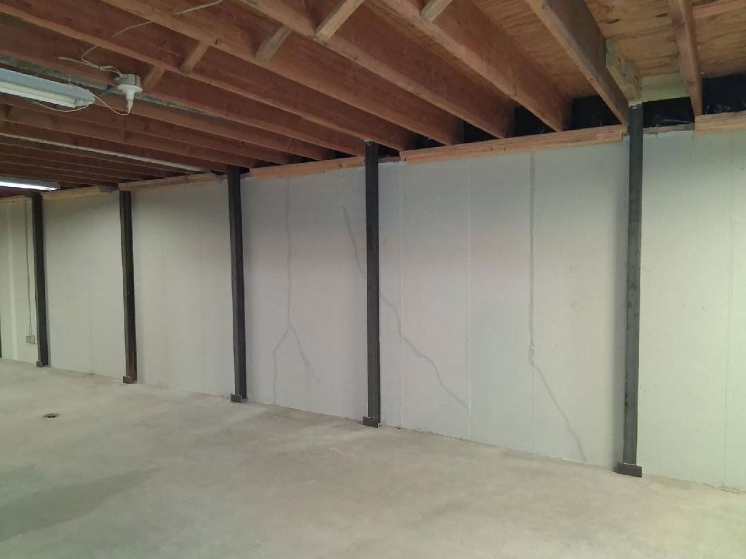 Basement interior with support beams. Gray walls, concrete floor, wooden ceiling beams.