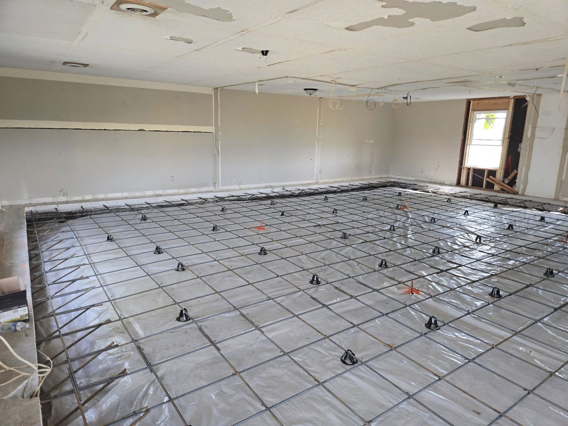 Room with rebar grid on plastic sheeting, prepped for concrete floor pour.