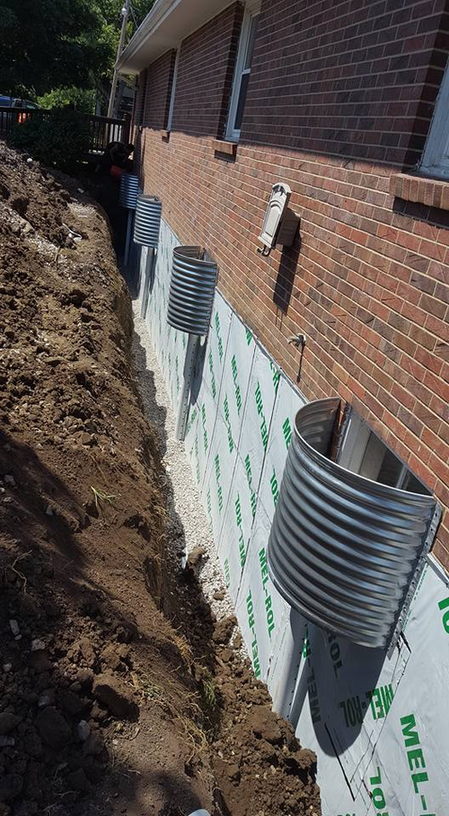 Workers installing metal edging on a wall, using a level and drill. White gloves, exterior setting.