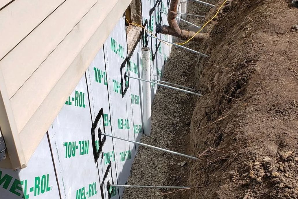Wall anchors installed through a foundation wall with protective moisture barrier into an adjacent trench.