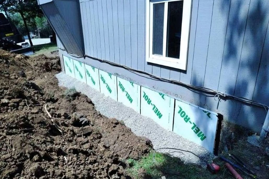 Person wearing yellow gloves applying sealant to a concrete surface, near a wall and grass.