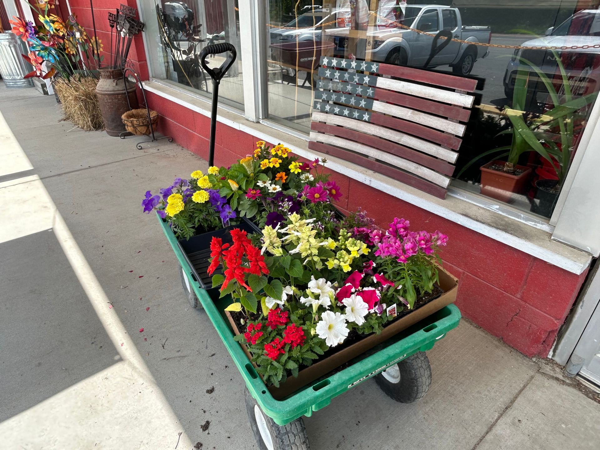 A green wagon filled with flowers is parked on the sidewalk in front of a store