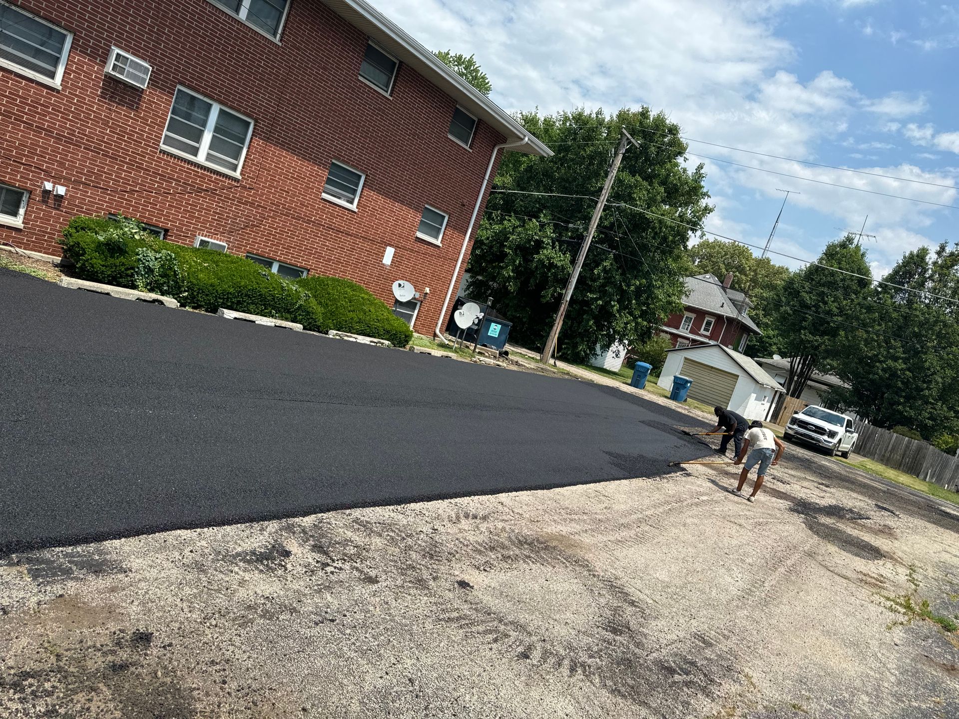 A group of people are working on a driveway in front of a brick building.