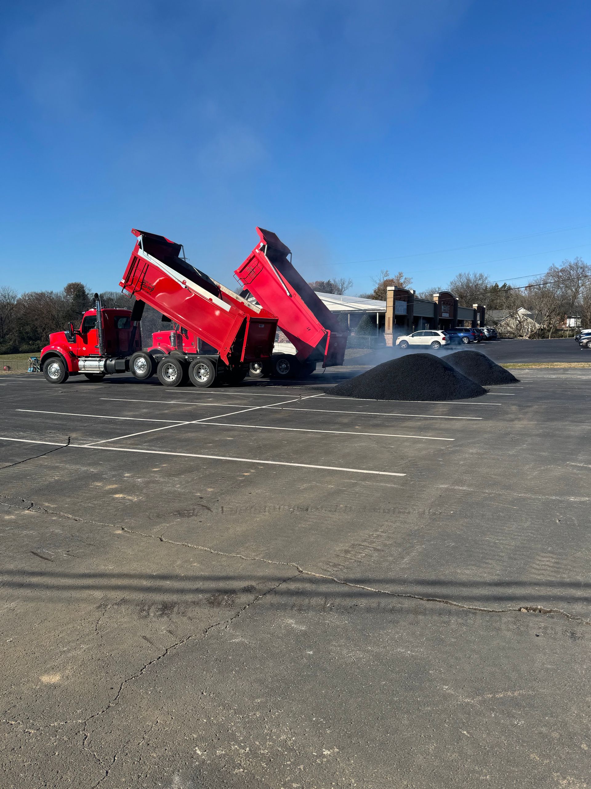 A red dump truck is dumping dirt into a parking lot.
