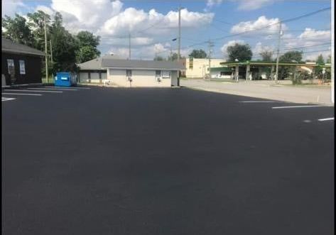 A parking lot with a building in the background and a blue dumpster in the foreground.