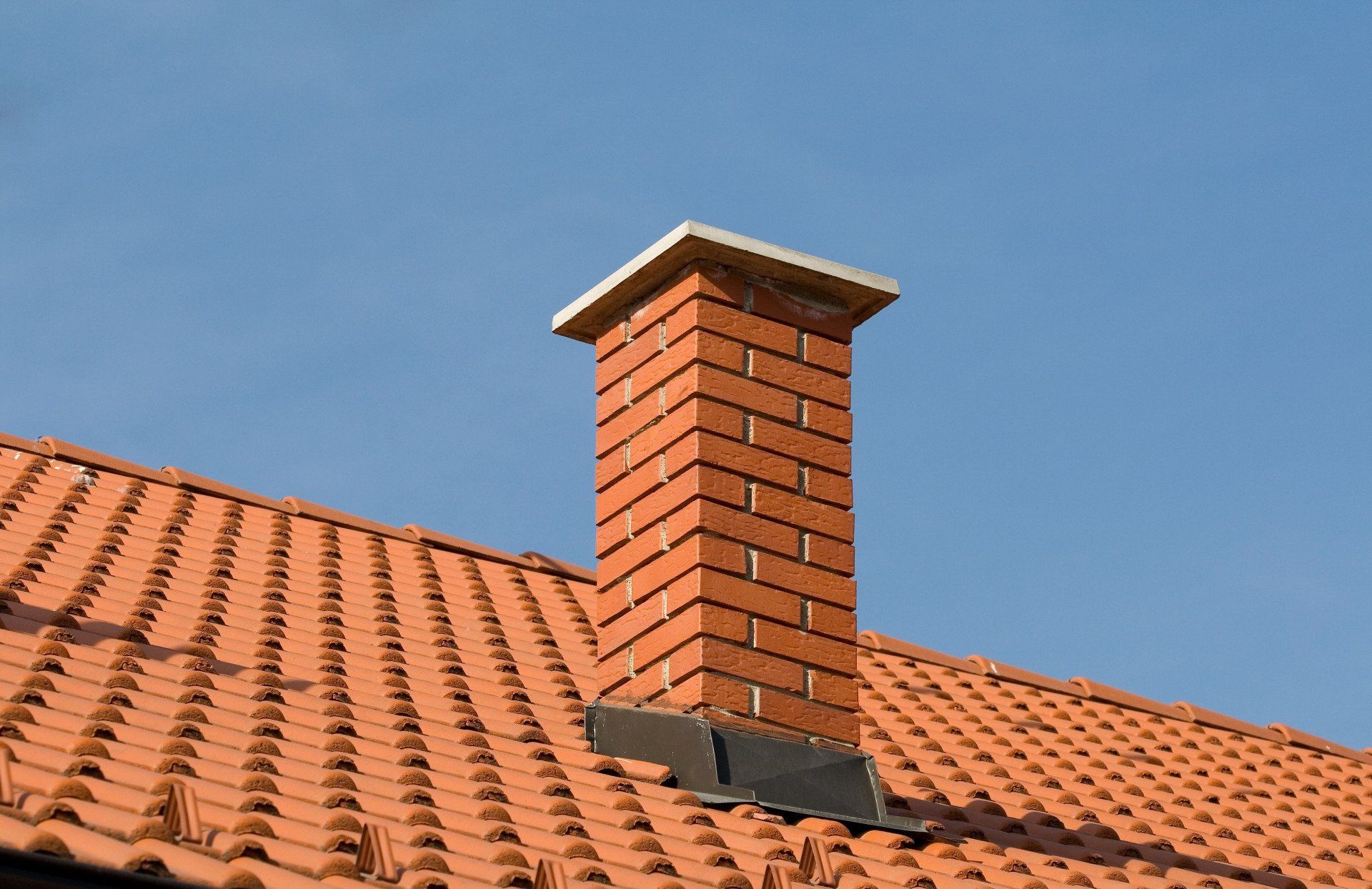 Brick chimney on a red tiled roof against a blue sky.