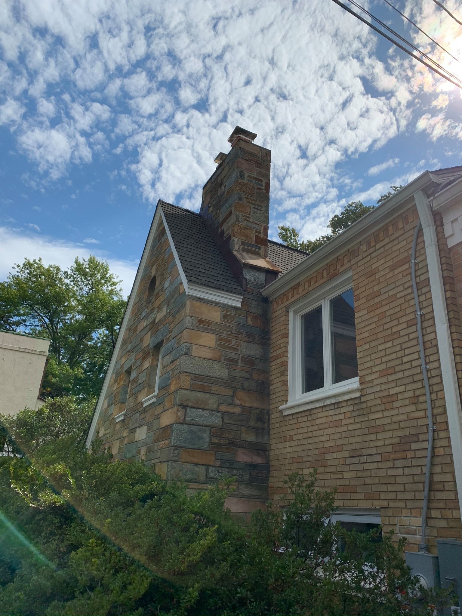 A brick and stone house with a chimney against a blue sky with clouds.