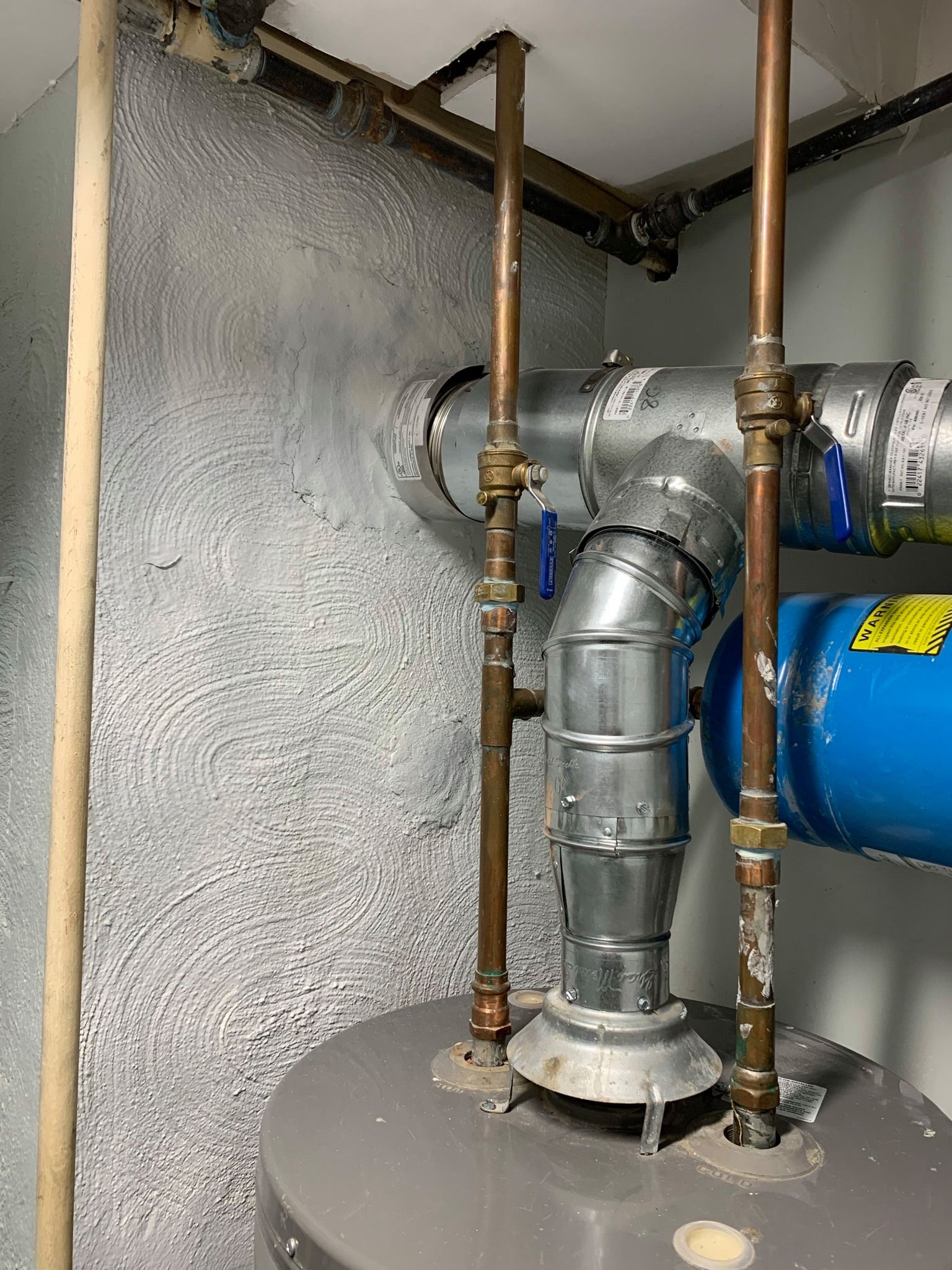 Water heater with copper pipes, a flue, and blue expansion tank in a basement.