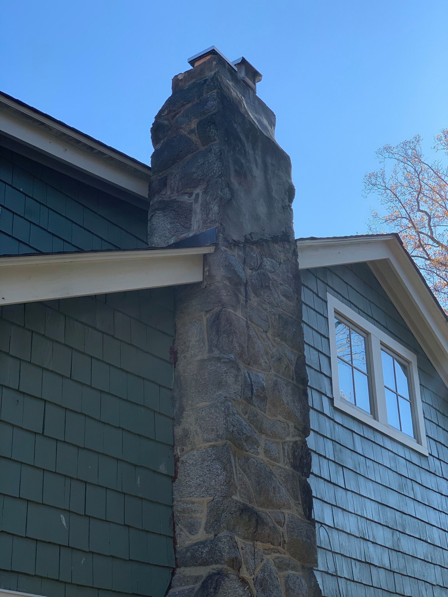 Stone chimney rising from a green-sided house against a blue sky.