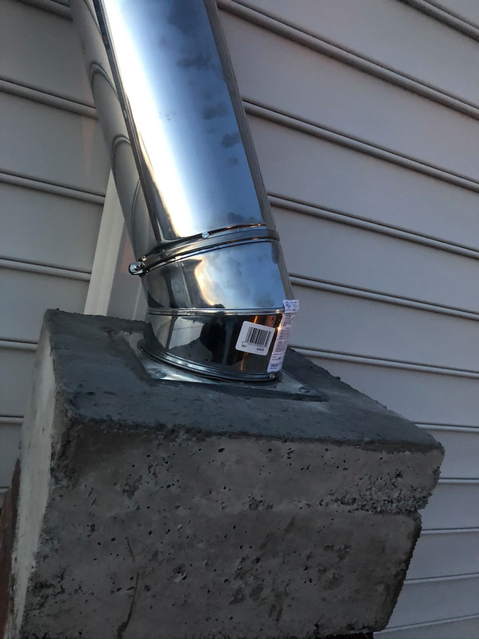 Metal chimney pipe attached to concrete base against a siding wall.