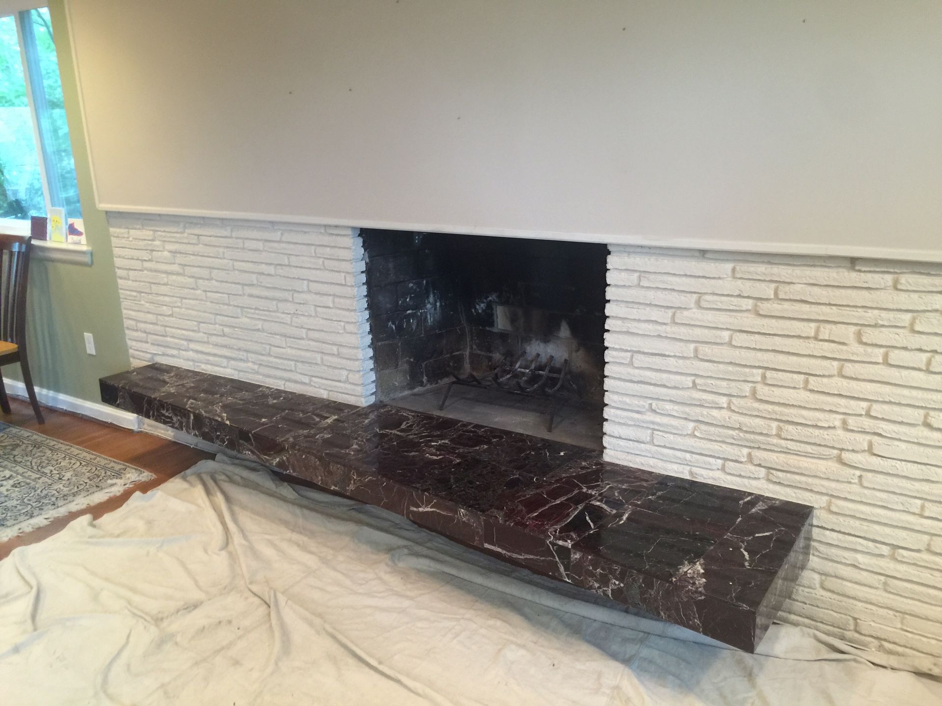 Fireplace with dark marble shelf, white brick, and blackened interior. A window and chair are visible.