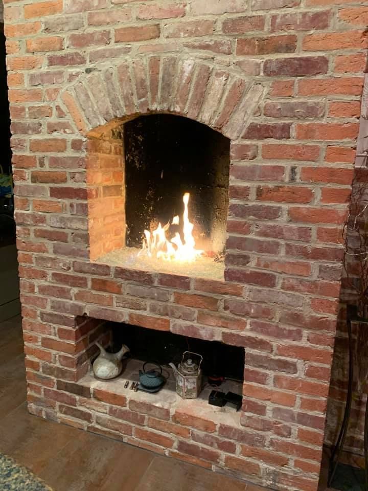 Brick fireplace with a lit fire in the opening.  Small lower opening has decorative items on the shelf.