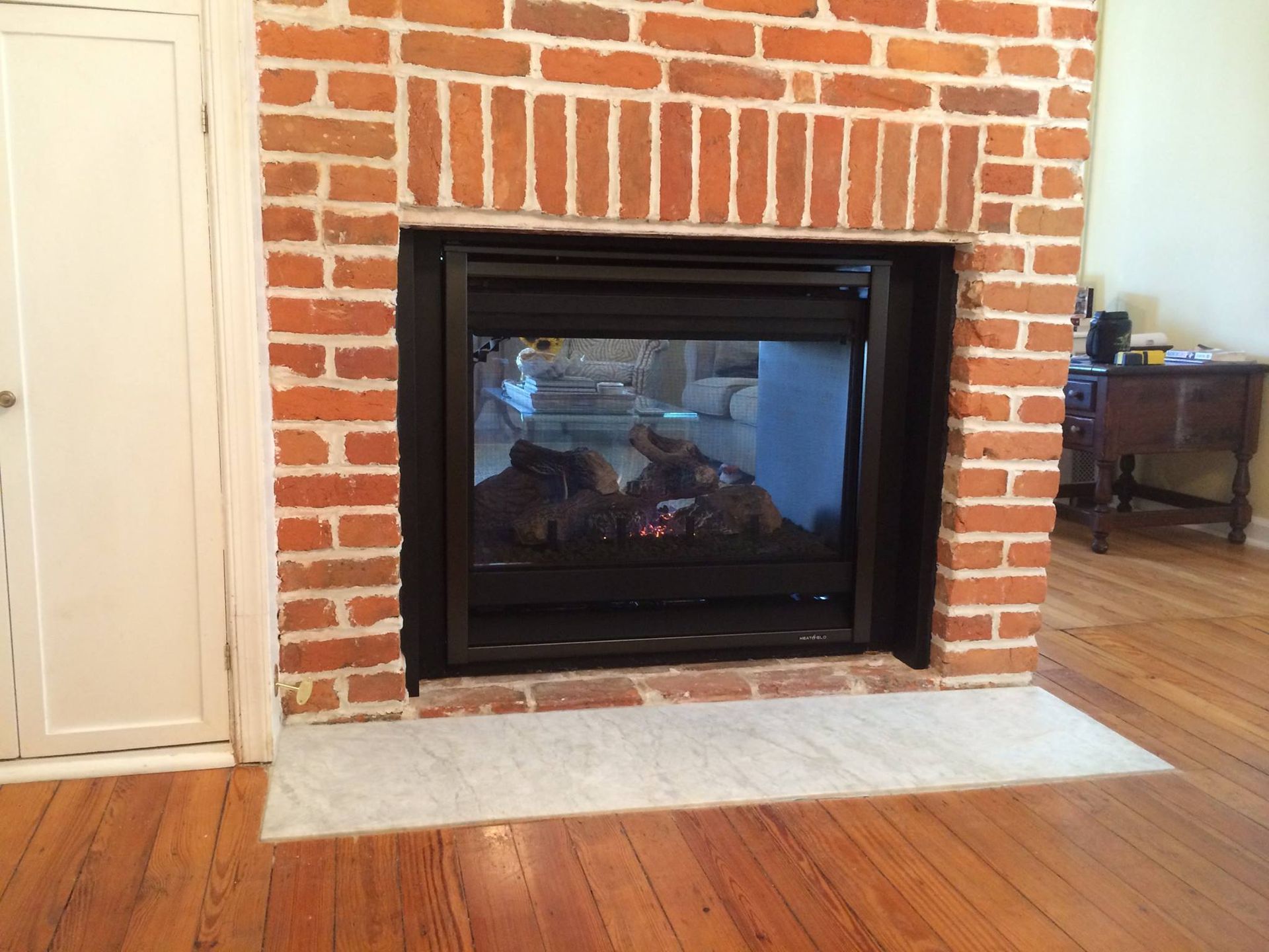 Fireplace with black frame in a brick wall, wood flooring, and white door.