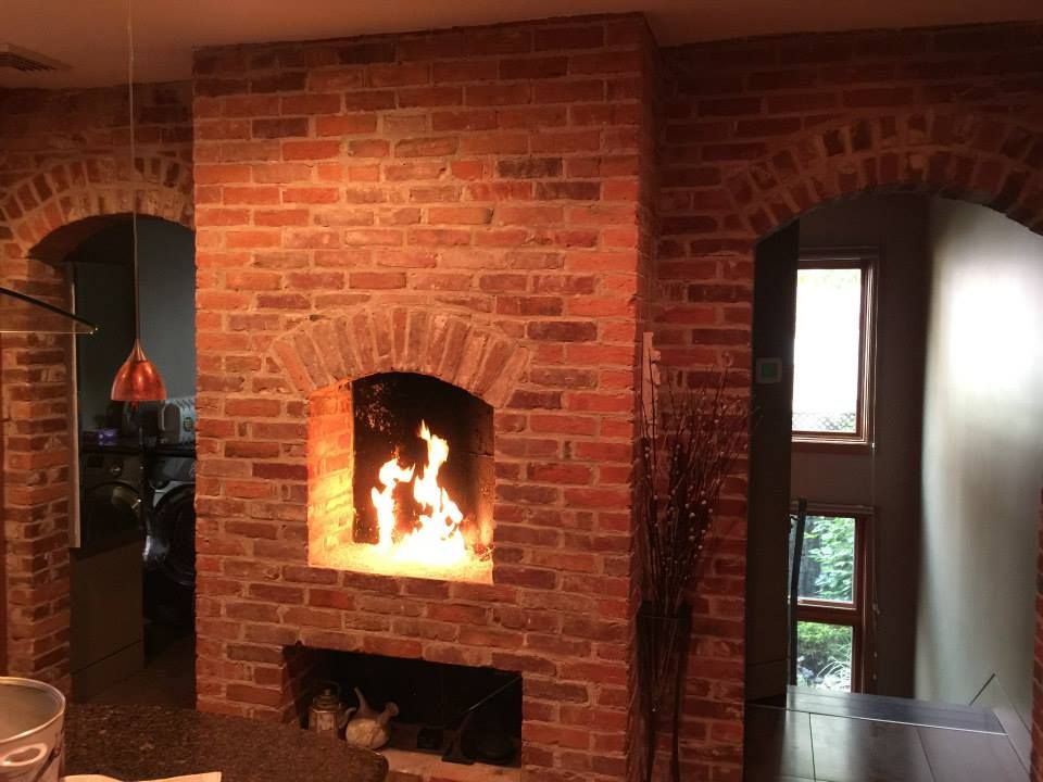 Brick fireplace with arched openings, lit fire, and adjacent room.