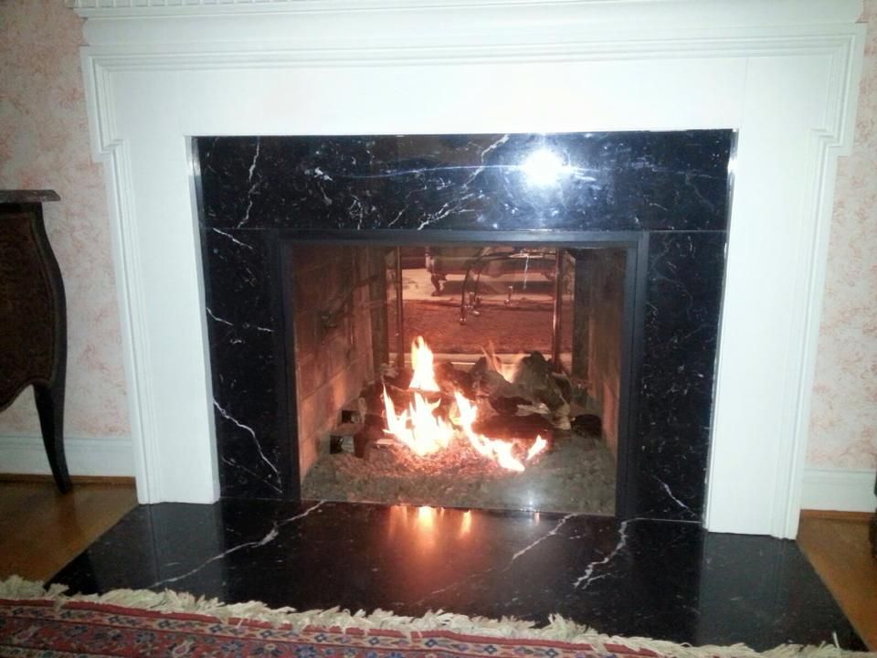 Fire burning in a fireplace with black marble surround and white mantel.