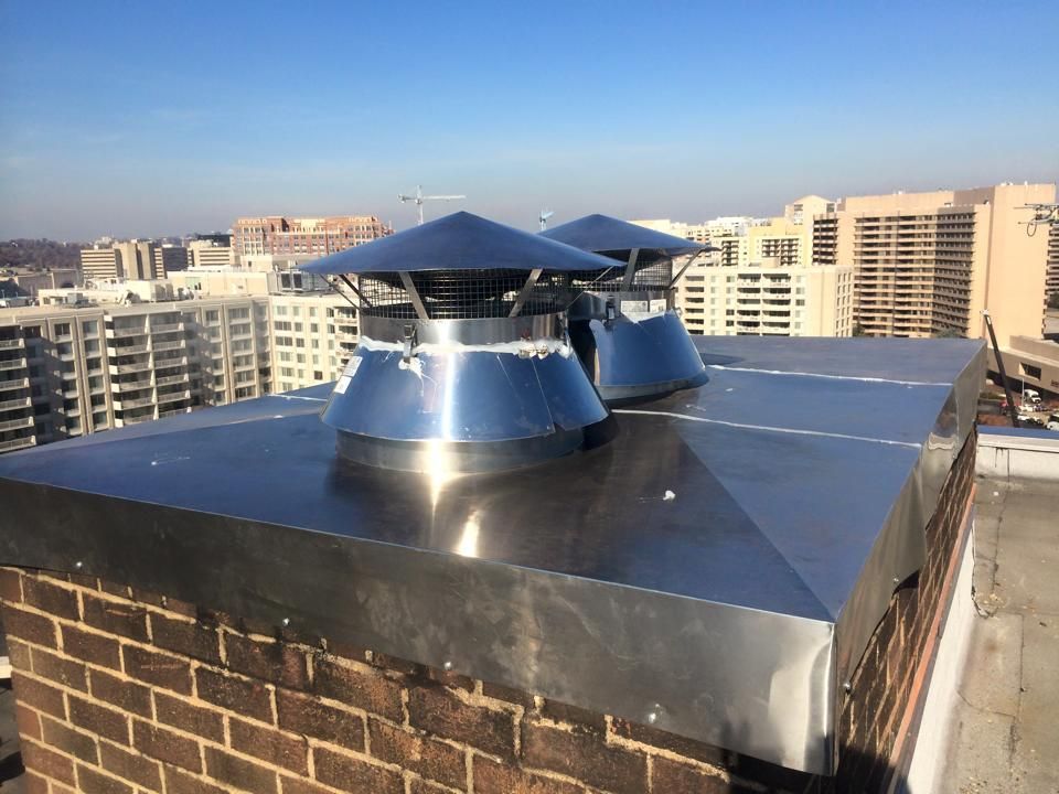 Two shiny metal chimney caps on a flat roof with a city skyline in the background.
