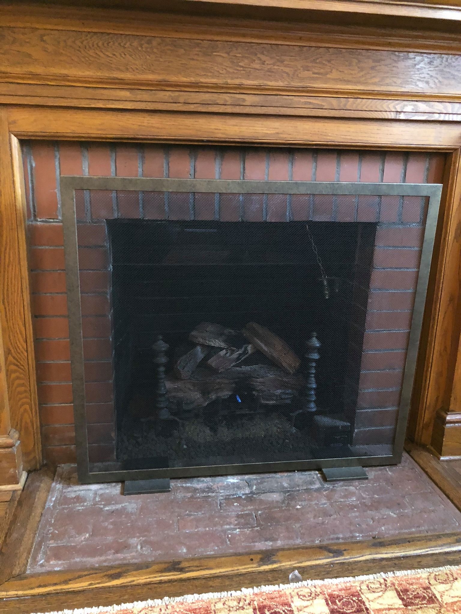 Fireplace with brick interior, mesh screen, and wooden mantel.