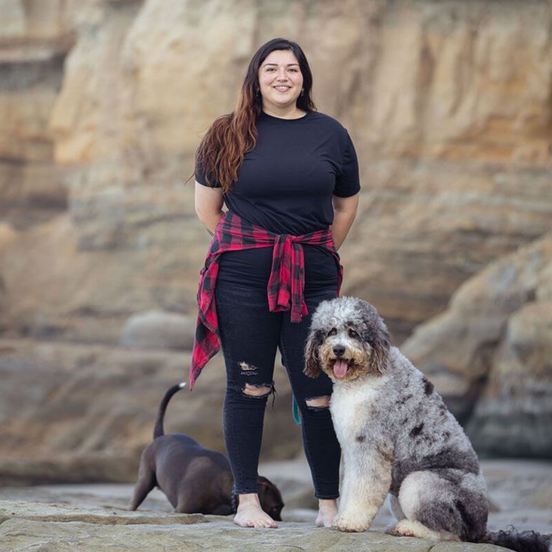 A woman is standing next to a dog on a rocky beach.