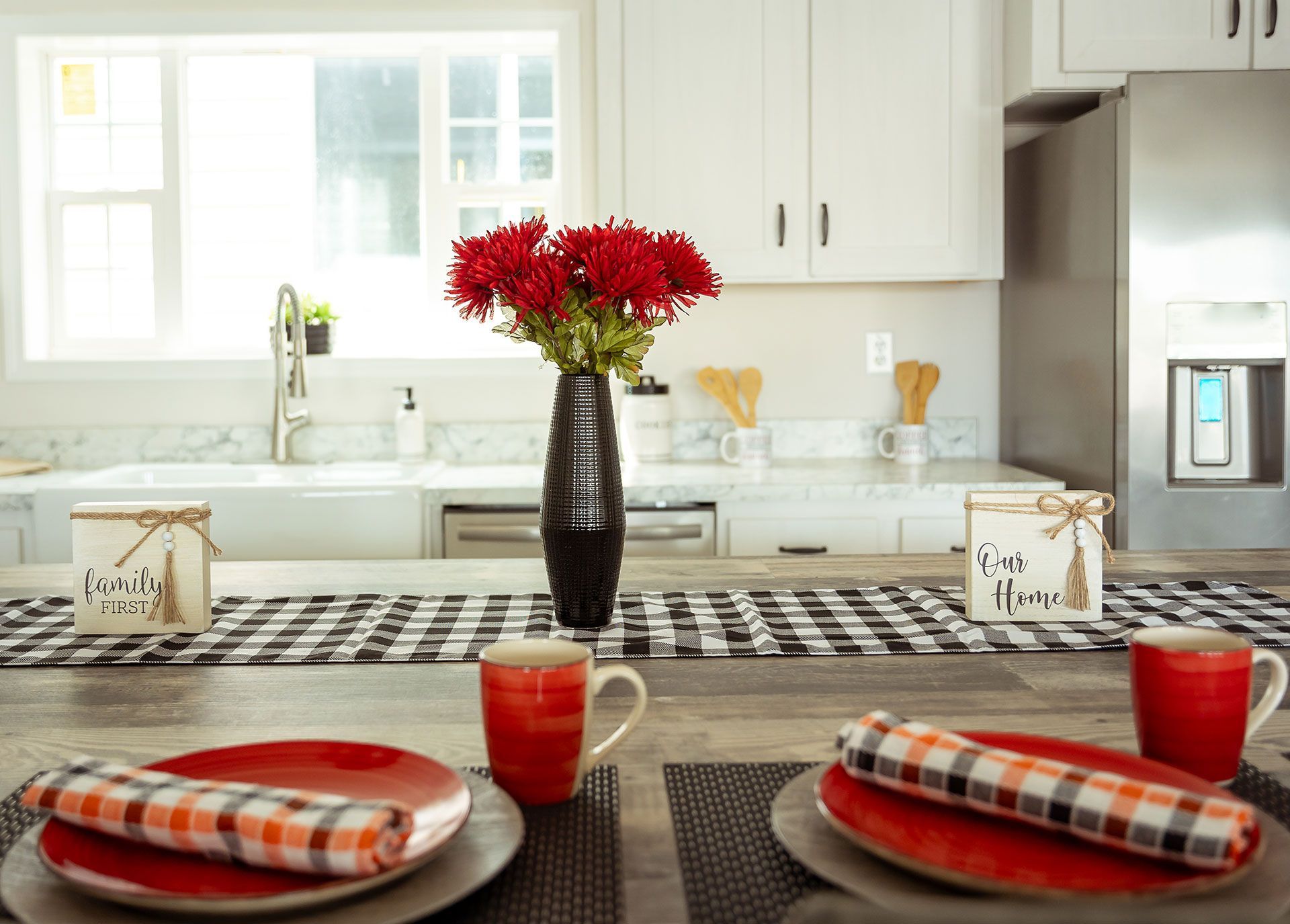 A kitchen with plates, cups, napkins, and a vase of flowers on the counter