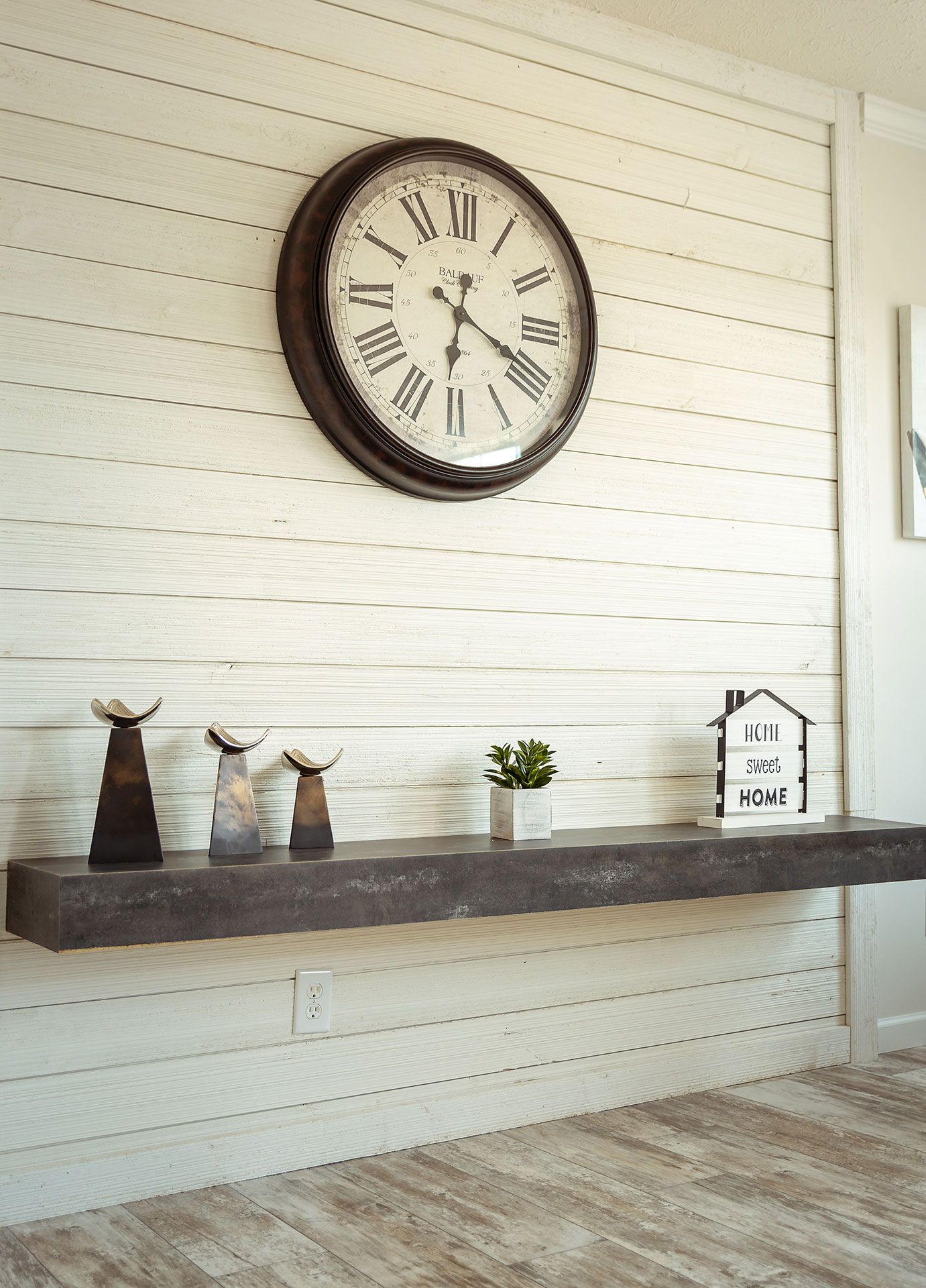 A large clock is hanging on a white wall above a shelf
