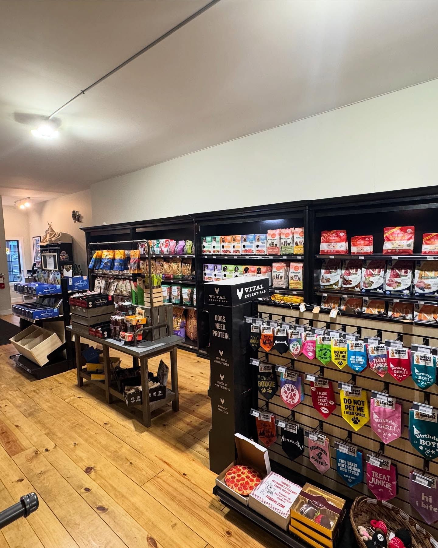 Interior of a pet supply store with wooden floors, featuring shelves stocked with pet food, treats, and accessories.