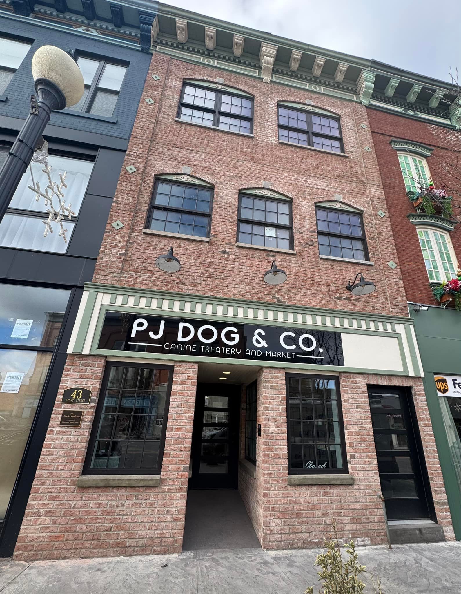Brick building with PJ DOG & CO. sign. Black-framed windows and doors. Green and white awning.