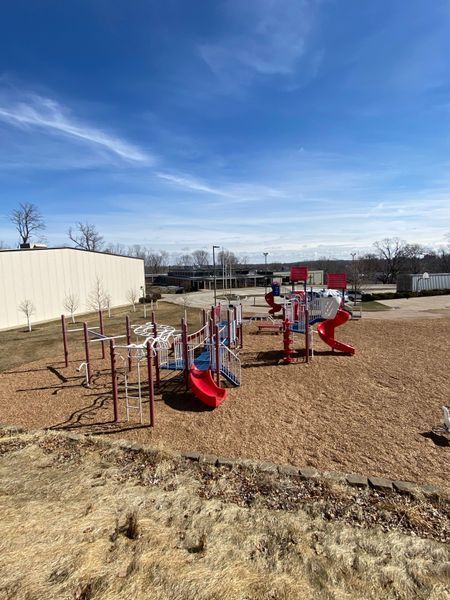 Playground with red, white, and blue equipment on wood chips under a blue sky.