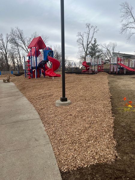 A playground with red and blue slides, covered in wood chips, next to a paved path.